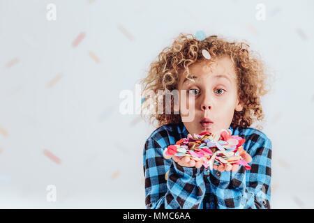 Junge blonde Junge holding Konfetti in den Händen und bläst es Stockfoto