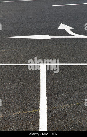 Eine abstrakte Anordnung für die weißen Linien und Pfeile auf dem schwarzen Asphalt auf einem Parkplatz Sandown Insel, weiß, UK. Stockfoto