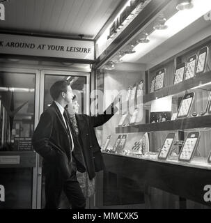 1960er Jahre, ein junger Erwachsener Paar stehen zusammen an der Ringe in einem schmuck shop Fenster, London, England, UK. Stockfoto