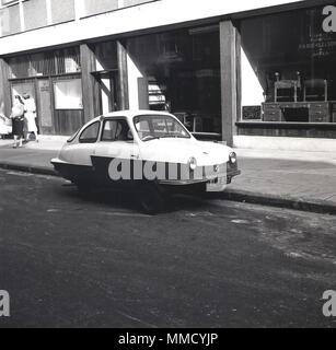 1960 s, unusua Suchen kleinen dreirädrigen Auto' in einer ruhigen Stadt London Nebenstraße geparkt gegenüber der Showrooms von Büromöbeln, Einzelhändler, F. eine Schnalle & Söhne. In den 50s und 60s, Dreirädern wurde populär, da sie leicht abgestellt werden und nicht eine separate Lizenz benötigen, wenn Sie ein Motorrad Lizenz verwendet. Stockfoto