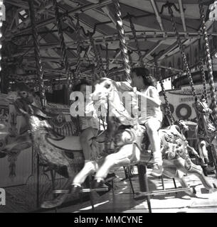 1960er Jahre, historisch, zwei junge Mädchen, die auf einem Karussell auf den Holzpferden reiten oder Karussell auf der lustigen Messe im Battersea Park, London, England, Großbritannien. Das Messegelände wurde für die Feierlichkeiten des Festival of Britain 1951 im nördlichen Teil des Parks gebaut und war viele Jahre lang eine wichtige Attraktion. Stockfoto