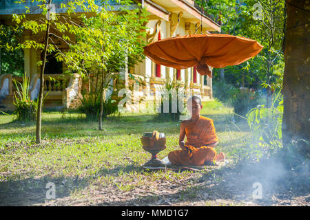 Krabi, Thailand - 2. Mai 2015: Anfänger Mönch meditieren auf Feld unter langstieligen Sonnenschirm in der Nähe von Buddhistischen Kirche in Krabi, Thailand Stockfoto