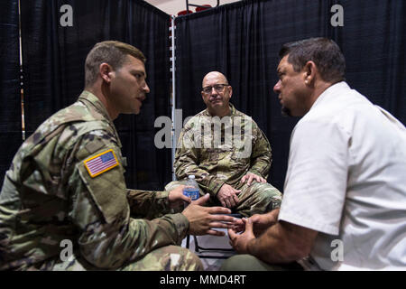 Us-Armee Kapitän Mark Johnston, Chaplin, 14 Combat Support Hospital, Gespräche mit einem lokalen Bewohner, während seine Familie Mitglied wird für eine Kopfverletzung behandelt, als Sgt. Brad Lemky, Behavioral Health, 14. CHS, übersetzt, was Er in Spanisch in Humacao Arena, wo der 14. CHS ihre Feldlazarett in Humacao Puerto Rico, Okt. 18, 2017 Satz sagt. Die 14 CSH ist die lokale Krankenhäuser, deren Fähigkeiten durch den Hurrikan Maria betroffen waren. (U.S. Air Force Foto von Airman 1st Class Nicholas Dutton) Stockfoto