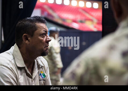 Us-Armee Kapitän Mark Johnston, Chaplin, 14 Combat Support Hospital, Gespräche mit einem lokalen Bewohner, während seine Familie Mitglied wird für eine Kopfverletzung behandelt, als Sgt. Brad Lemky, Behavioral Health, 14. CHS, übersetzt, was Er in Spanisch in Humacao Arena, wo der 14. CHS ihre Feldlazarett in Humacao Puerto Rico, Okt. 18, 2017 Satz sagt. Die 14 CSH ist die lokale Krankenhäuser, deren Fähigkeiten durch den Hurrikan Maria betroffen waren. (U.S. Air Force Foto von Airman 1st Class Nicholas Dutton) Stockfoto