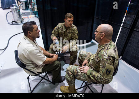 Us-Armee Kapitän Mark Johnston, Chaplin, 14 Combat Support Hospital, Gespräche mit einem lokalen Bewohner, während seine Familie Mitglied wird für eine Kopfverletzung behandelt, als Sgt. Brad Lemky, Behavioral Health, 14. CHS, übersetzt, was Er in Spanisch in Humacao Arena, wo der 14. CHS ihre Feldlazarett in Humacao Puerto Rico, Okt. 18, 2017 Satz sagt. Die 14 CSH ist die lokale Krankenhäuser, deren Fähigkeiten durch den Hurrikan Maria betroffen waren. (U.S. Air Force Foto von Airman 1st Class Nicholas Dutton) Stockfoto
