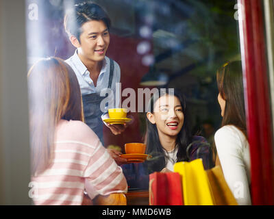 Jungen asiatischen Kellner weiblichen Kunden im Coffeeshop serviert, Schuß durch Fensterglas. Stockfoto