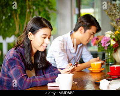 Zwei jungen asiatischen erwachsene Mann und Frau im Café sitzen, spielen mit dem Handy. Stockfoto