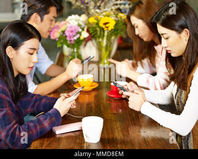 Vier jungen asiatischen erwachsene Männer und Frauen im Café sitzen, spielen mit Handy mit sehr ernsten Gesichtsausdruck. Stockfoto