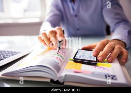 Unternehmer mit Handy beim Schreiben Zeitplan im Tagebuch Stockfoto