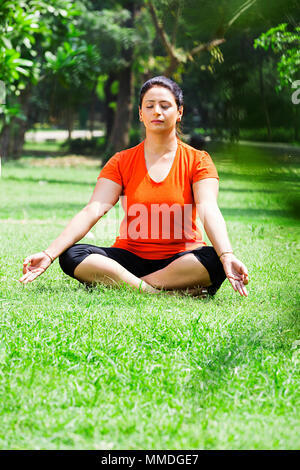 Eine Frau sitzt Park Yoga Padmasana Praxis Meditation Übung Stockfoto