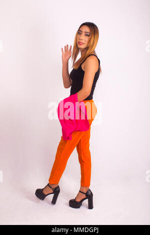 Seite Pose der Frau in orange Hosen, schwarze Bluse und rote Jacke winkt für Kamera Stockfoto