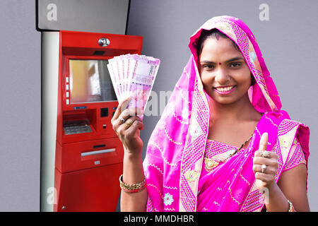 Eine ländliche Weiblichen angezeigt Thumbs-up mit Indischen Rupien Geldautomaten Bargeld beziehen Stockfoto