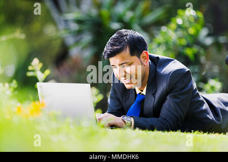 Ein Unternehmer Mitarbeiter liegende Gras Ausruhen mit Laptop arbeiten In - Garten Stockfoto