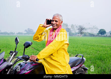 Eine ländliche Dorfbewohner alter Mann reiten Motorrad und Reden Handy Feld Stockfoto