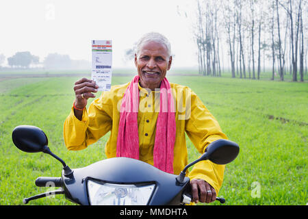 Eine ländliche Dorfbewohner alte Mann sitzt Scooter Übersicht Aadhaar-Card Regierung - Feld "Identität" bezeichnet ist. Stockfoto