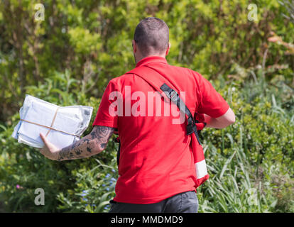 Die britische Royal Mail Postbote Holding eine Handvoll Buchstaben beim Gehen durch einen Park an einem sonnigen Tag in England, Großbritannien. Stockfoto