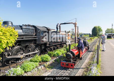 Kleine und große Konzept bei der britischen Museumsbahn. Vintage UK Dampflok nimmt Wasser Seite an Seite mit Miniatur-eisenbahn für Kinder reiten. Stockfoto