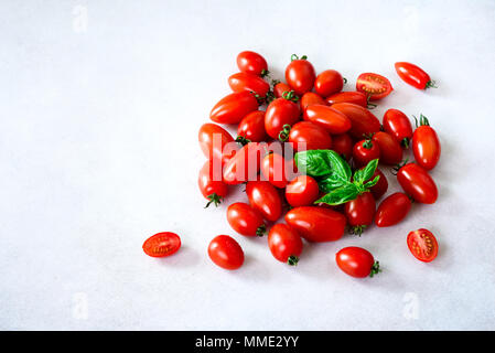 Kirschtomate auf grauem Hintergrund mit Copyspace. Rot, Gelb und Schwarz, Tomaten, Basilikum Stockfoto