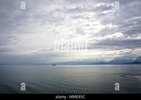 Cook Inlet, Alaska, USA: ein Frachter auf dem Horizont gegen Berge in Nebel gehüllt, mit dichten, dramatische Wolken Overhead. Stockfoto