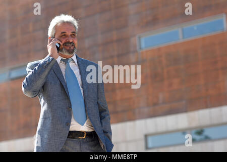 Portrait eines älteren Geschäftsmann im Gespräch mit einem Smart Phone außerhalb der modernen Bürogebäude. Erfolgreicher Geschäftsmann im städtischen Hintergrund. Stockfoto