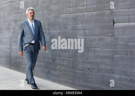 Senior Geschäftsmann zu Fuß außerhalb der modernen Bürogebäude. Erfolgreiche Mann mit Anzug und Krawatte im städtischen Hintergrund. Stockfoto