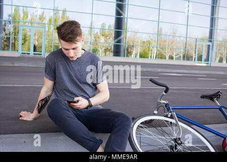 Junge Hipster mit Handy, fixed Gear Bike auf Stadt Straße. großer Spiegel windows Hintergrund, städtische Fahrrad Fahrer Stockfoto