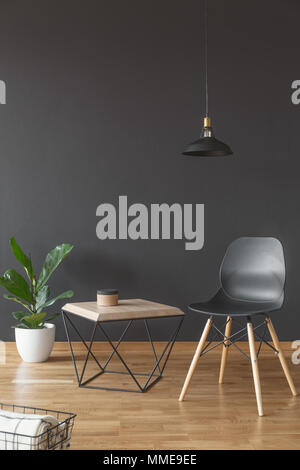 Pflanze, einfacher Stuhl und Holz Couchtisch auf Schwarz, leere Wand im Wohnzimmer Innenraum