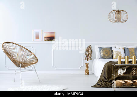 Goldene Sessel, Doppelbett mit Kissen, Decke und Fotos an der Wand im Schlafzimmer Innenraum Stockfoto
