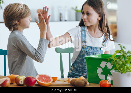 Geschwister hohe Fiving, während die Trennung biologisch abbaubare Abfälle in der Küche Stockfoto