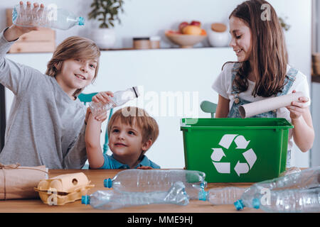Lächelnde Kinder Spaß haben, während die Trennung von Plastikflaschen und Papier in einem grünen bin Stockfoto