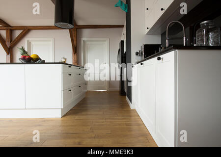 Low Angle View einer modernen Küche Einrichtung mit Holzfußboden, weißen Schränke und Arbeitsplatte schwarz Stockfoto