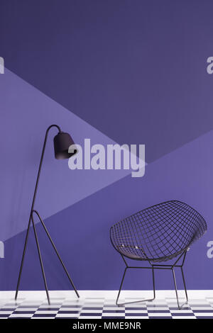 Asymmetrische Violet Wand in einem modernen Wohnzimmer Interieur mit Metall Lampe und schwarzen Sessel auf kariertem Boden. Real Photo Stockfoto