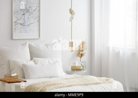 Einfache Lampe Lampe auf einem Seil über dem Bett mit weißer Bettwäsche, Bücher und gold Farn Blatt auf ein Ende der Tabelle in Weiß Schlafzimmer Innenraum hängen Stockfoto