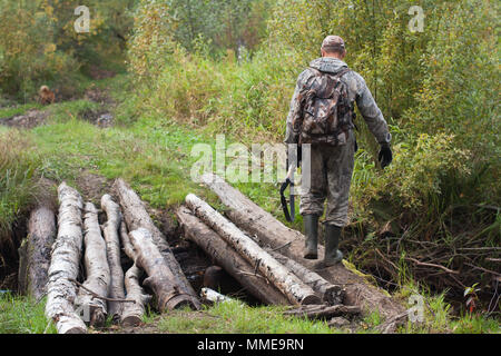 Jäger mit Flinte durchquert den Wald Fluss auf der Brücke Stockfoto