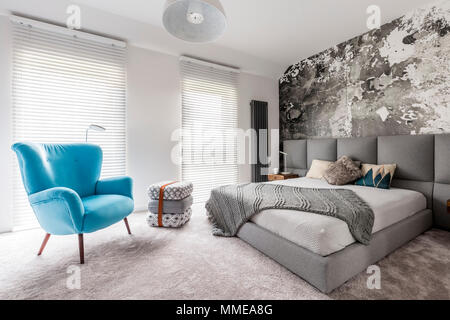 Einfarbig grau Schlafzimmer mit grunge Wand, Holz- Nachttisch, weiße Wände und blaue Sessel Vintage Style Stockfoto