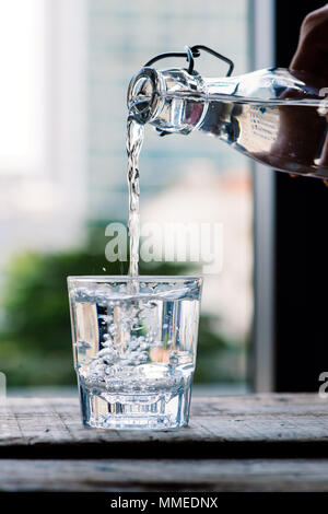 Sauberes Trinkwasser ist aus einer Kanne in einem runden Glas Schale goß auf einem Holztisch und ein hellgrün Serviette Nahaufnahme Makro auf eine grüne Natur Stockfoto