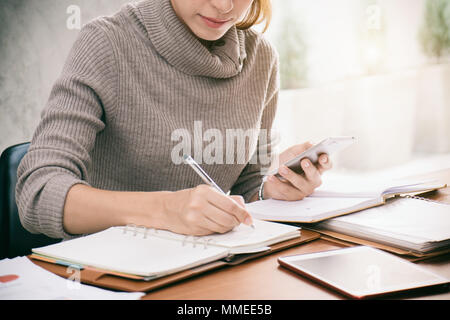 Porträt einer schönen jungen Geschäftsfrau, Sitzen im Büro, Mobiltelefon. Stockfoto