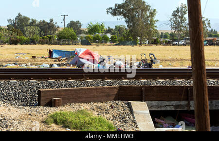 Obdachlose Camp, Eisenbahnschienen, ländlichen Kern County Road, verstreuten Müll, eingezäunt Unterteilung im Hintergrund. Stockfoto