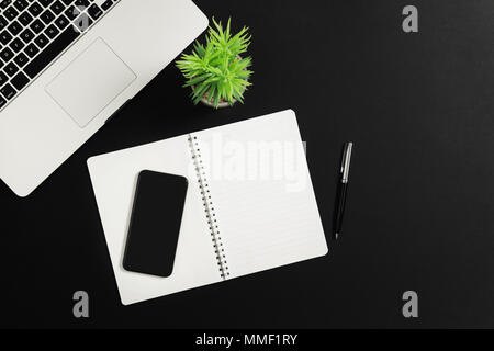 Bürotisch Schreibtisch mit Laptop, Smartphone und Notebook auf schwarzem Hintergrund. Ansicht von oben. Stockfoto