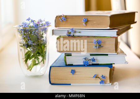 Einen Stapel Bücher mit kleinen blauen Blumen zwischen den Seiten auf weißen Tisch Stockfoto