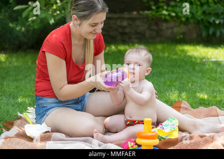 Schöne junge Frau, die Flasche zu Ihrem Baby auf Outdoor Familie Picknick im Park Stockfoto