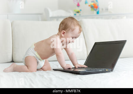 Cute Baby boy in Windeln kriechen auf dem Bett in Richtung Laptop Stockfoto