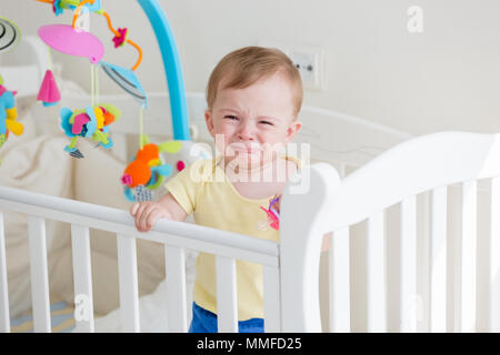 Portriat von 10 Monate alten Baby im Babybett und Weinen Stockfoto