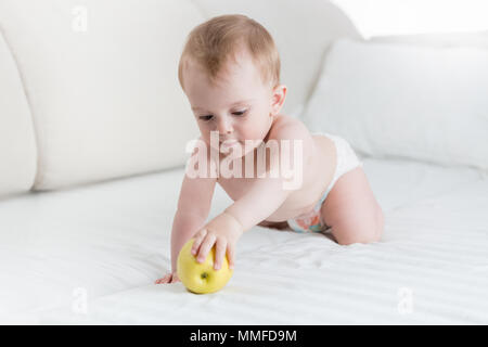 Portrait von 10 Monate alten Baby boy Kriechen auf Bett und unter großen gelben Apple Stockfoto