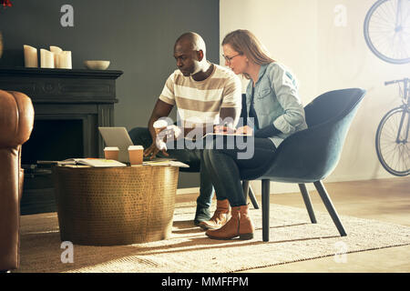 Zwei verschiedene junge Kollegen sitzen in einem stilvollen, modernen Office online gemeinsam mit einem Laptop Stockfoto