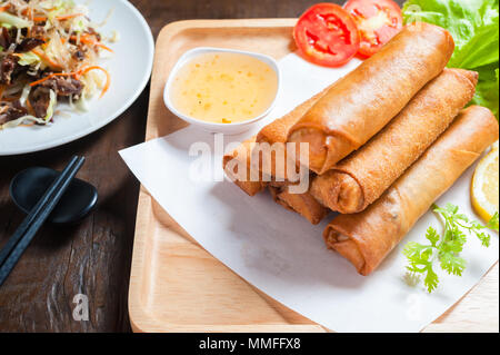 Knusprig gebratene Frühlingsrollen mit Pflaumen Soße und Salat, Zitronenscheiben auf hölzernen Tisch Stockfoto