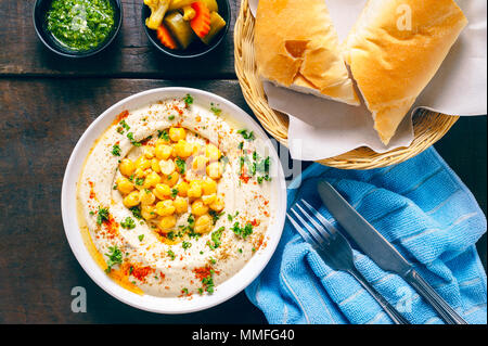 Israelische hummus cremig-Salat auf weiße Schüssel mit Kichererbsen, Olivenöl, Petersilie und Paprika. Mit Brot auf hölzernen Tisch serviert. Stockfoto