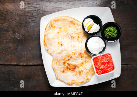 Frische thin ungesäuertes Brot mit gekochtem Ei, Salat Creme, Tomatensauce. In weißer Teller serviert und auf hölzernen Tisch zubereitet. Israelische Essen, Roti Stockfoto