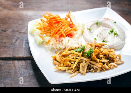 Chicken Shawarma oder Döner Kebab mit Hummus und Gemüse in weißer Teller serviert auf hölzernen Tisch. Stockfoto