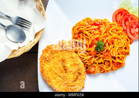 Weiße Platte leckere Spaghetti mit Schnitzel oder knusprig gebratenes Huhn, Petersilie Kartoffeln und Soße mit Tomaten und Gurke auf Holz- t in Scheiben geschnitten Stockfoto